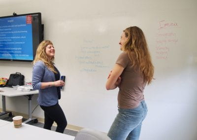 Two women in front of a white board talking